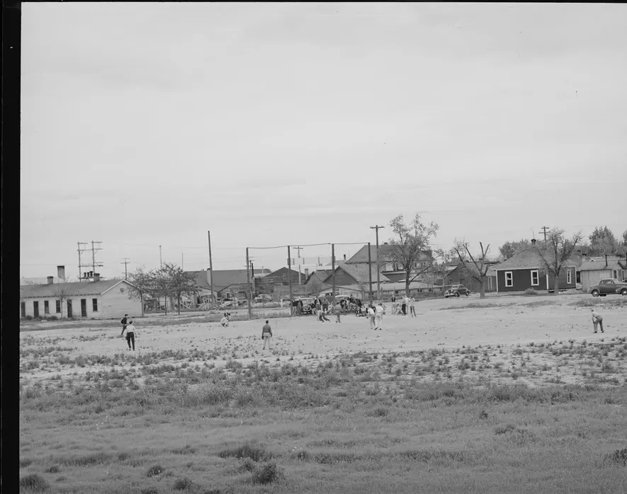 A sandlot baseball game on open ground at the edge of a small town, 1940s