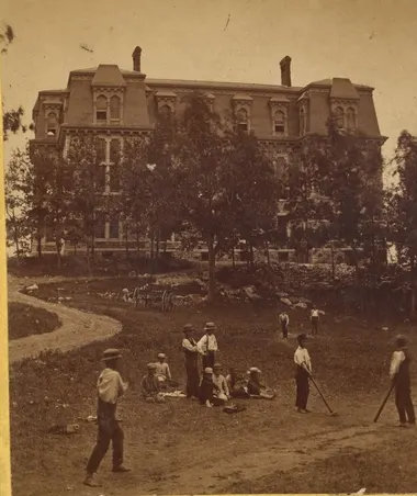 Boys playing baseball on a lawn before a large building, 19th-century stereograph